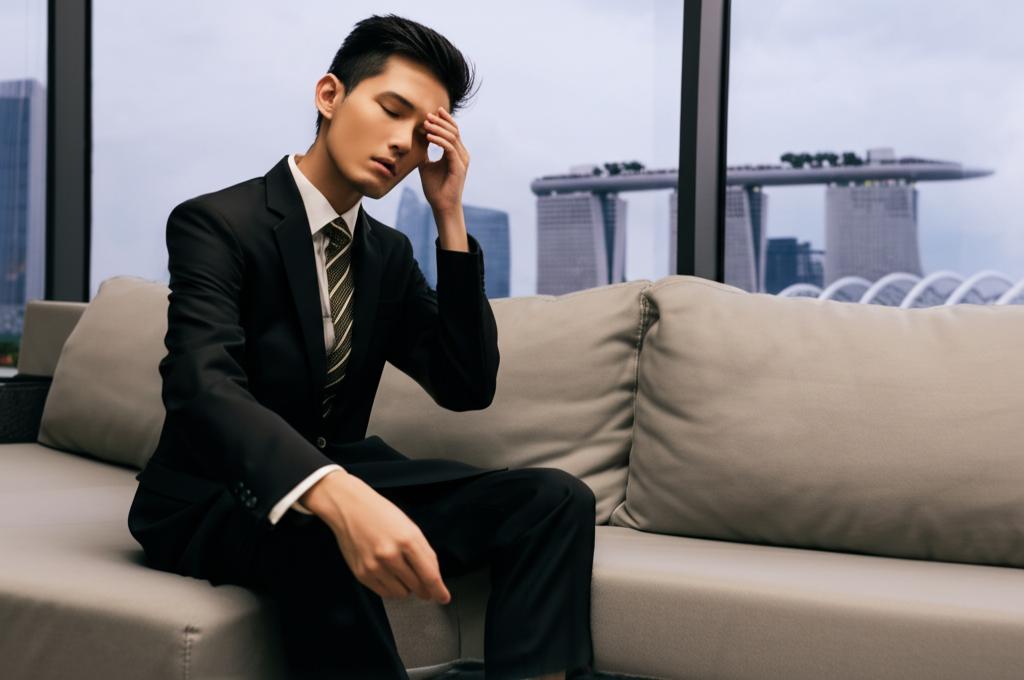 a tired asian office worker man sitting on a couch looking stressed, singapore cityscape background, realistic photo